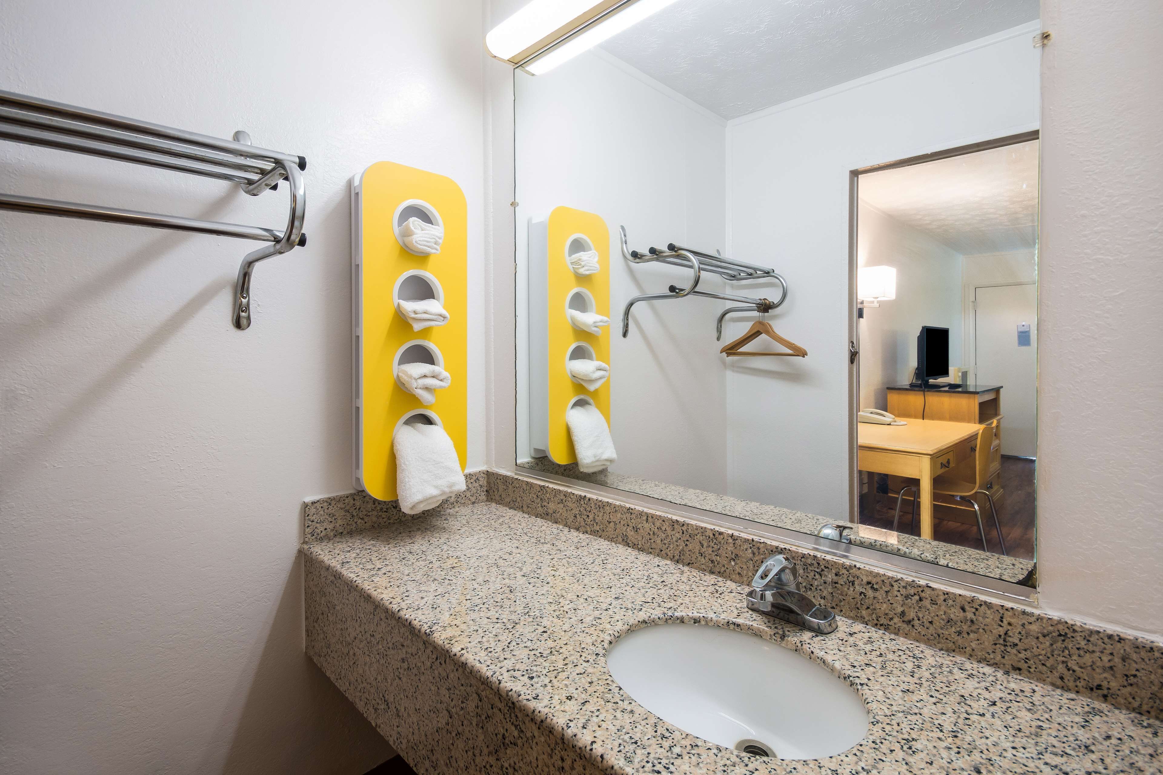 A bathroom with a granite countertop, a sink, a mirror, and towel dispensers.
