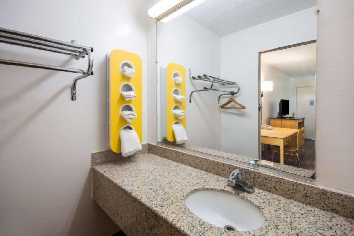 A bathroom with a granite countertop sink, a mirror, and a towel dispenser.