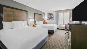 A hotel room with two beds, a desk, a television, and a window with curtains.