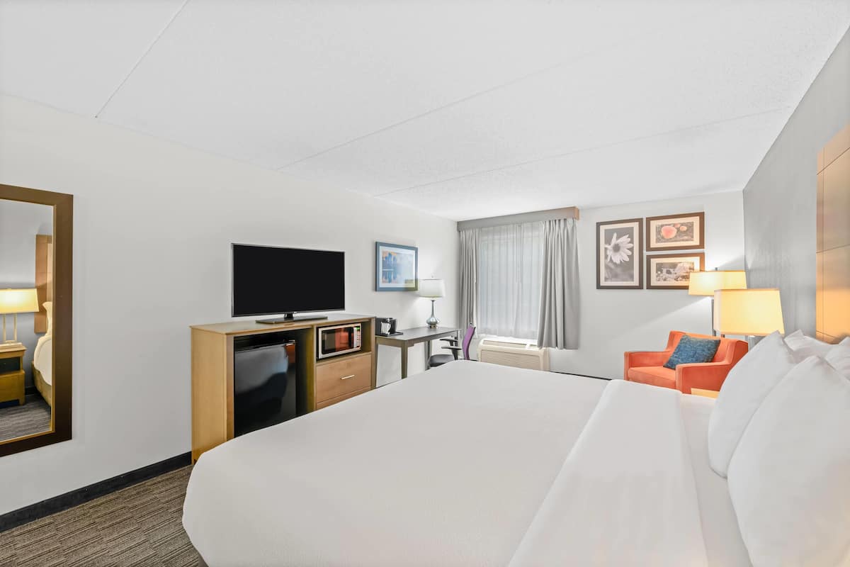 Habitación de hotel con una cama grande, un escritorio con televisor de pantalla plana, cómoda, una silla y una ventana con cortinas.