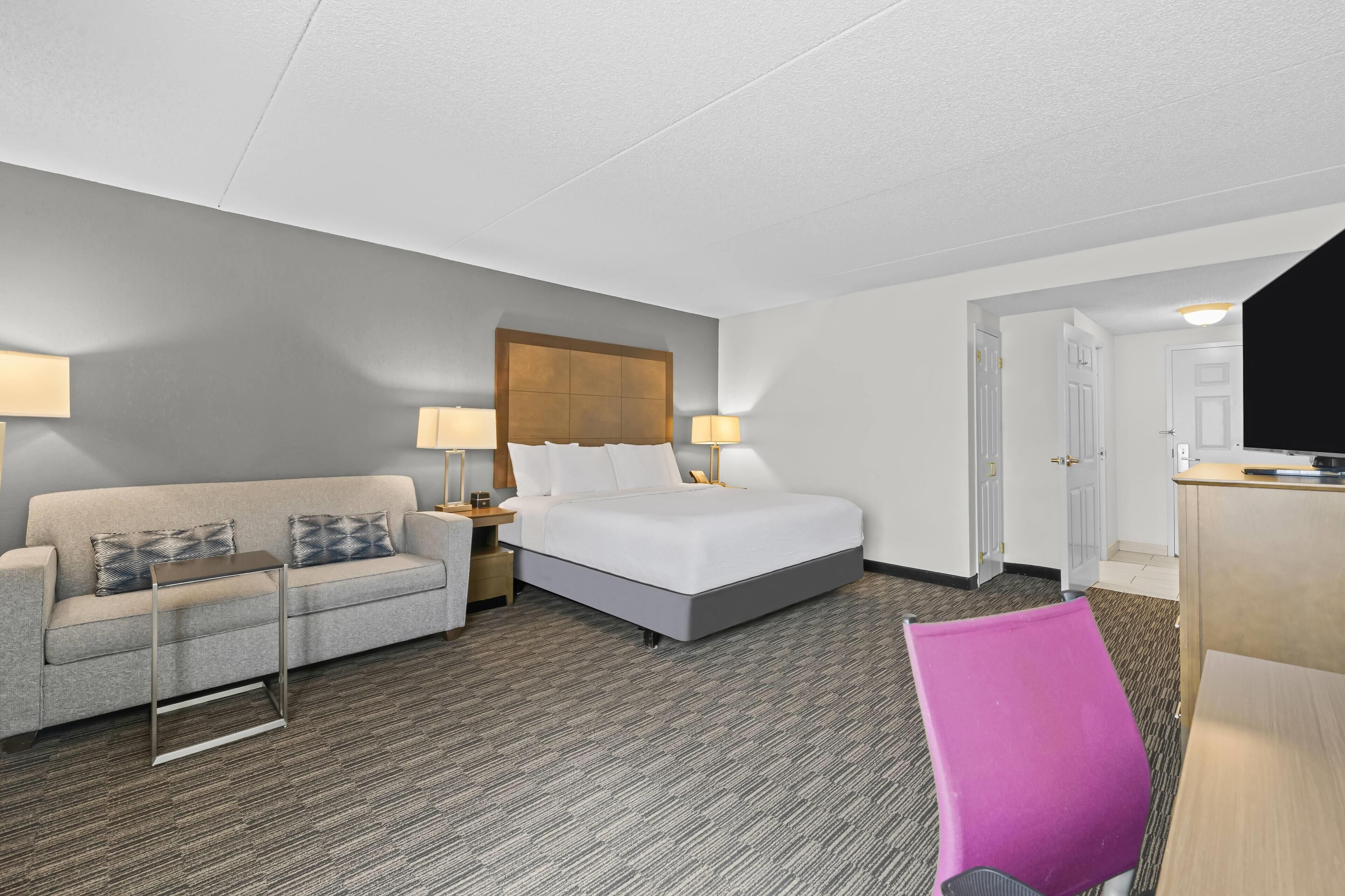 A hotel room with a bed, a sofa, a desk, and a chair.
