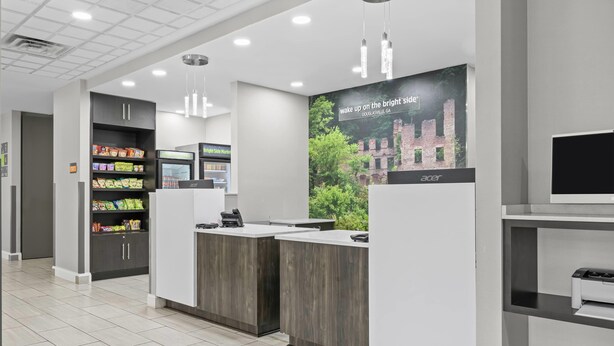 A modern reception area with a counter, a digital kiosk, and a printer. There is a sign with a city name and a slogan.