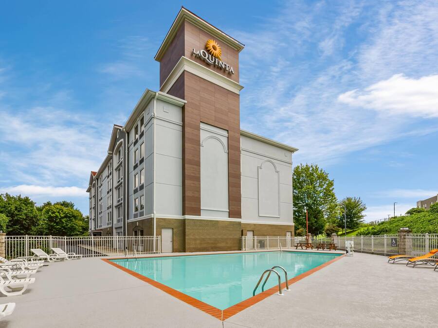 A hotel with a swimming pool, lounge chairs, and a clear blue sky.