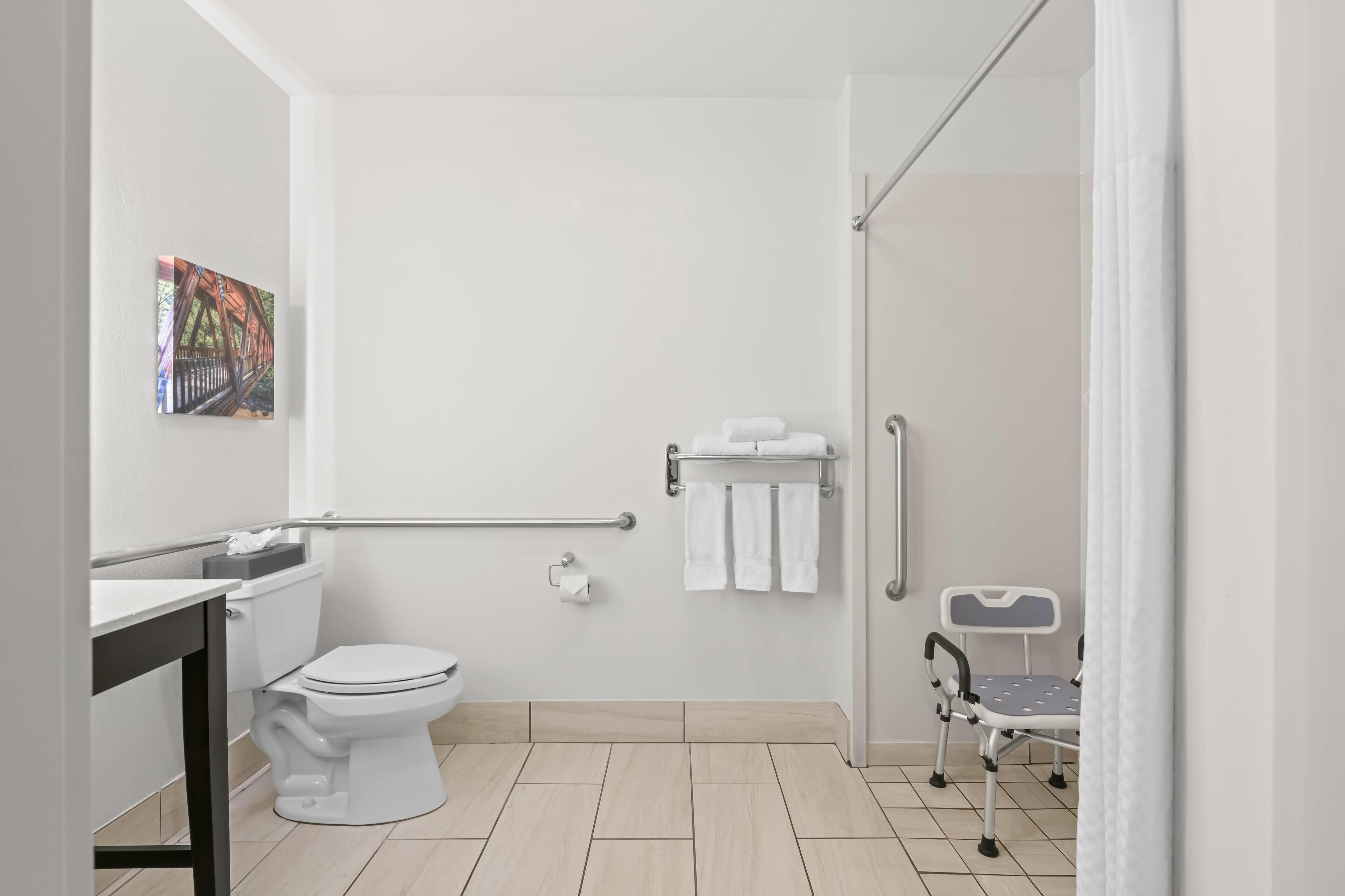 A modern bathroom with a toilet, bidet, towel rack, and a wheelchair-accessible chair.