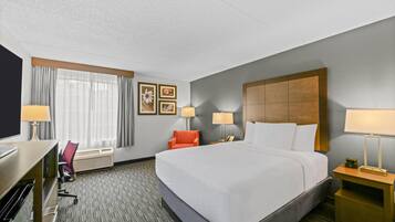 A hotel room with a large bed, two bedside tables with lamps, a desk with a chair, and a television.