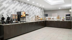 A modern kitchen area with a counter, coffee machines, and a refrigerator.