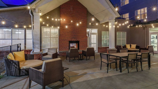Un espacio al aire libre con patio, chimenea de ladrillo, mobiliario de mimbre e iluminación con guirnaldas.