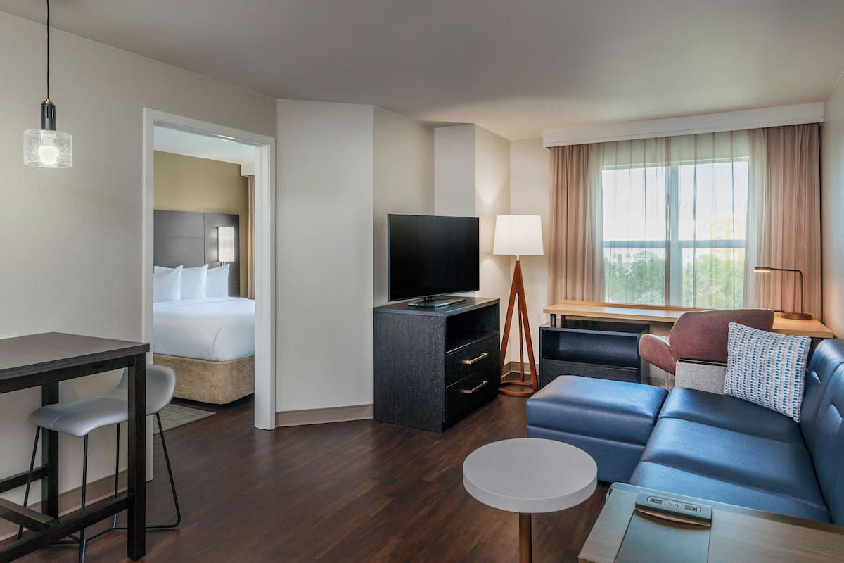 A modern hotel room with a bed, a TV, a desk, a sofa, and a small table.