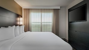 Una habitación de hotel con una cama grande, un televisor de pantalla plana en la pared y una ventana con cortinas.