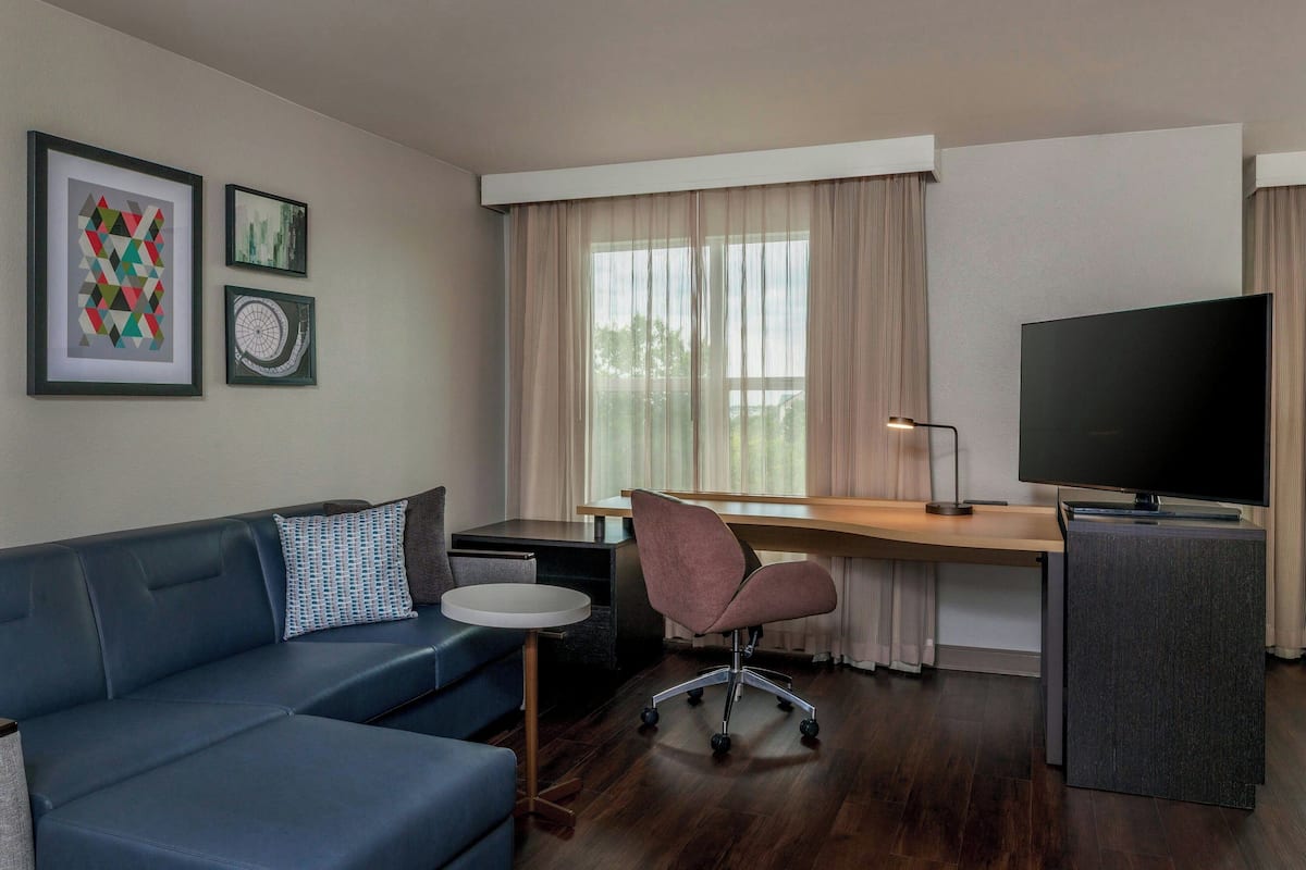 A modern room with a blue sofa, a desk with a computer, a TV, and framed artwork on the wall.