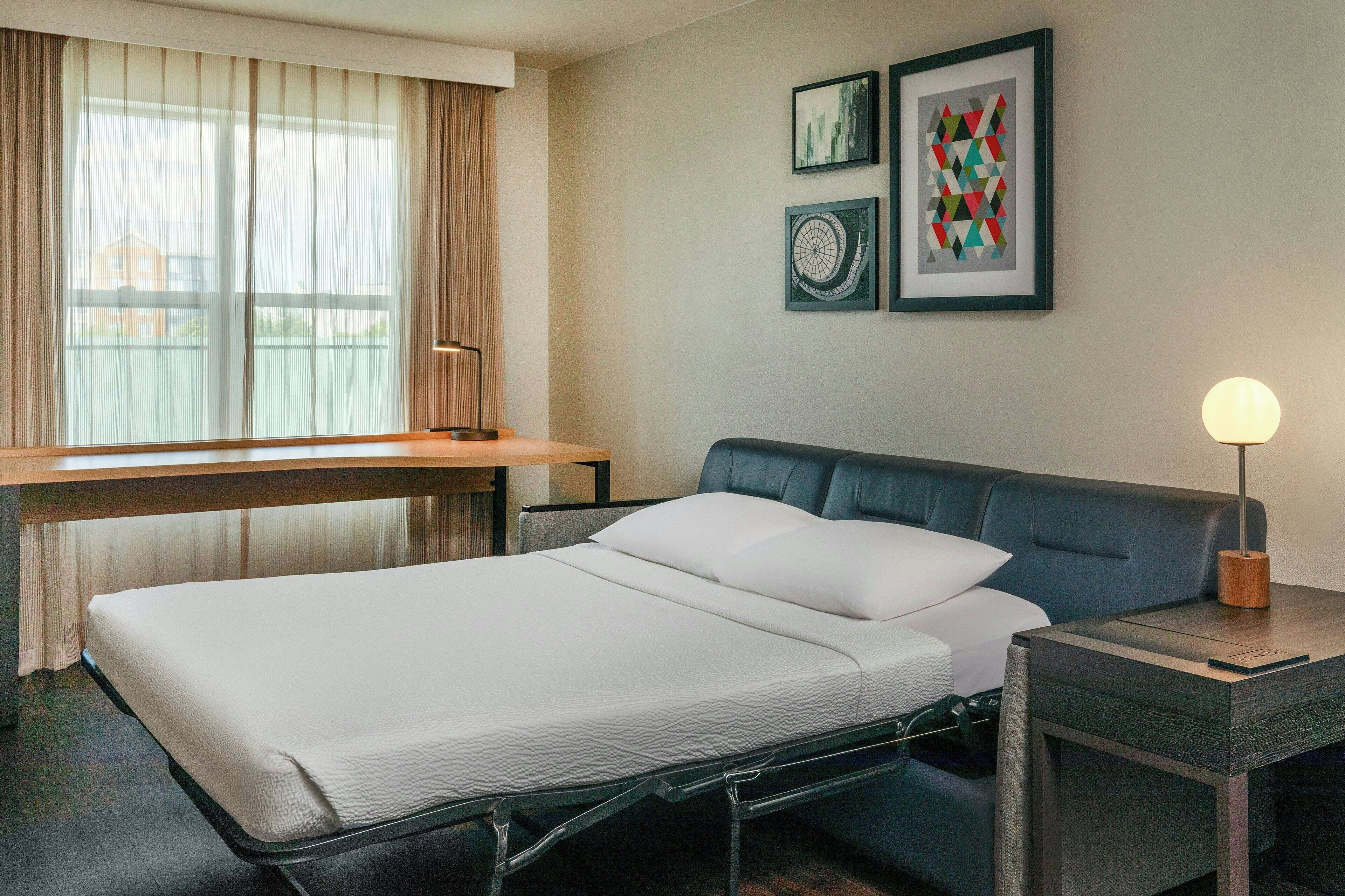 Una habitación de hotel moderna con una cama, una mesita de noche, una lámpara y obras de arte en la pared.
