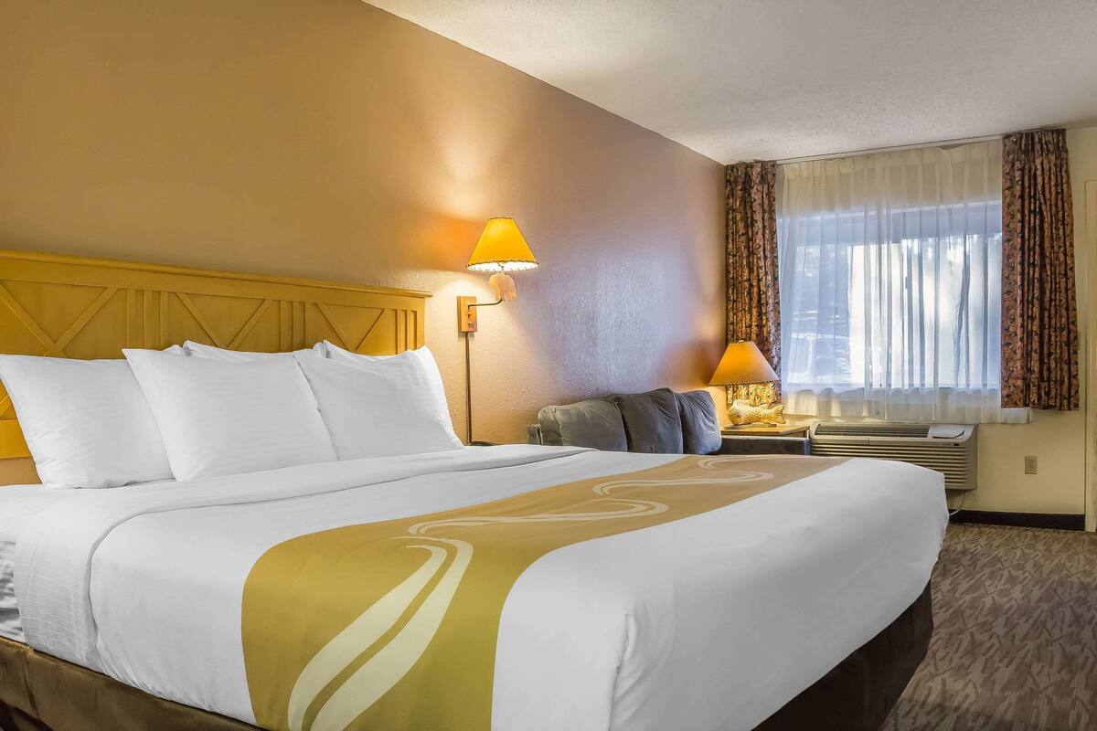 Una habitación de hotel con una cama grande, dos lámparas de noche, una ventana con cortinas y un equipo de aire acondicionado.