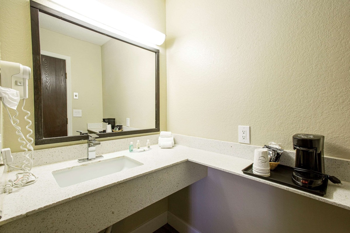 Un baño de hotel con lavamanos, espejo, toallero y una cafetera sobre el mostrador.