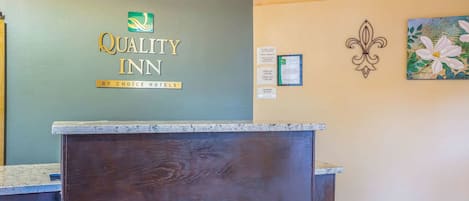 A reception desk with a logo for Quality Inn by Choice Hotels, a plaque, and a floral painting on the wall.