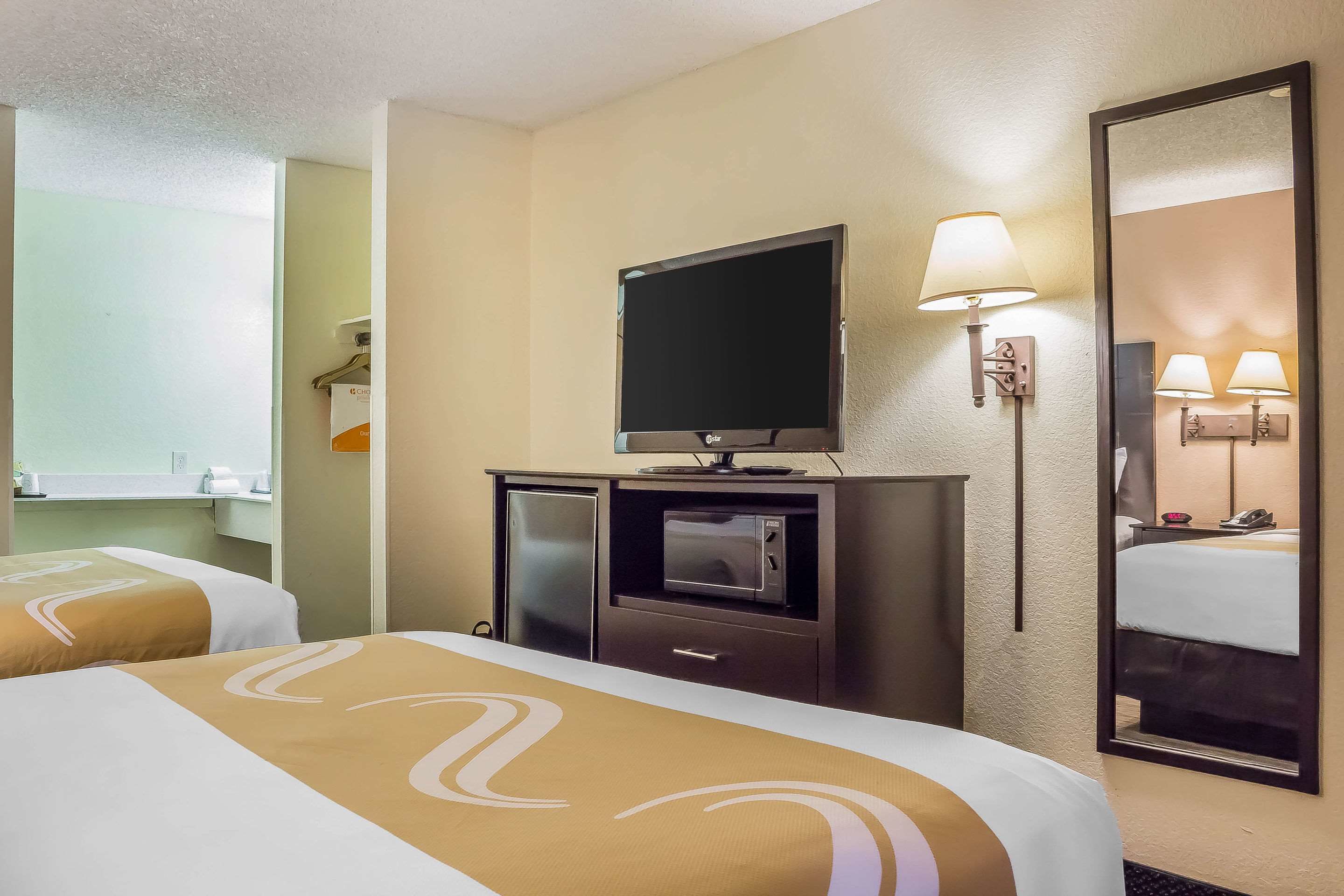 A hotel room with two beds, a TV, a microwave, and a mirror.