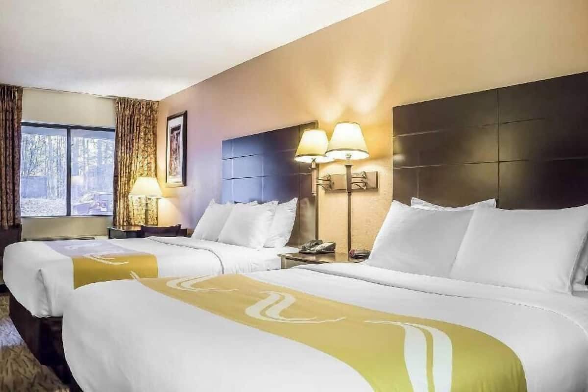 Una habitación de hotel con dos camas, un ventanal grande, un cabecero y dos lámparas de noche.