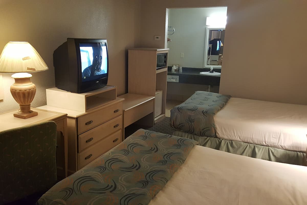 Ein Hotelzimmer mit zwei Betten, einem Schreibtisch mit Fernseher und einem Spiegel.