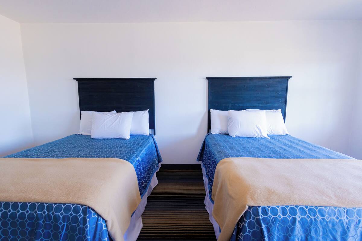 Ein Hotelzimmer mit zwei Betten, jeweils mit einer blauen, gemusterten Tagesdecke und weißen Kissen.