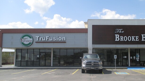 A parking lot with a truck in front of a building with a sign for TruFusion and The Brooke Hotel. - The Brooke Hotel (Brookshire)