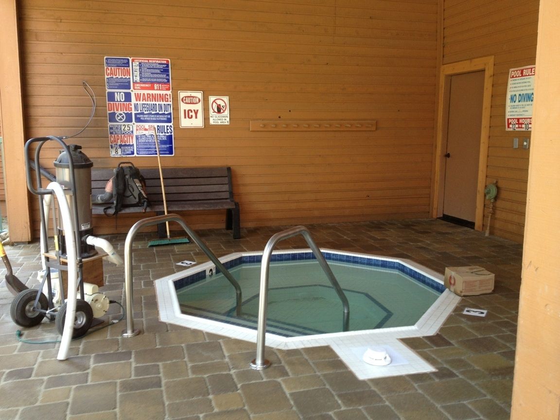 A small indoor pool with a wooden wall, a bench, and various safety signs.