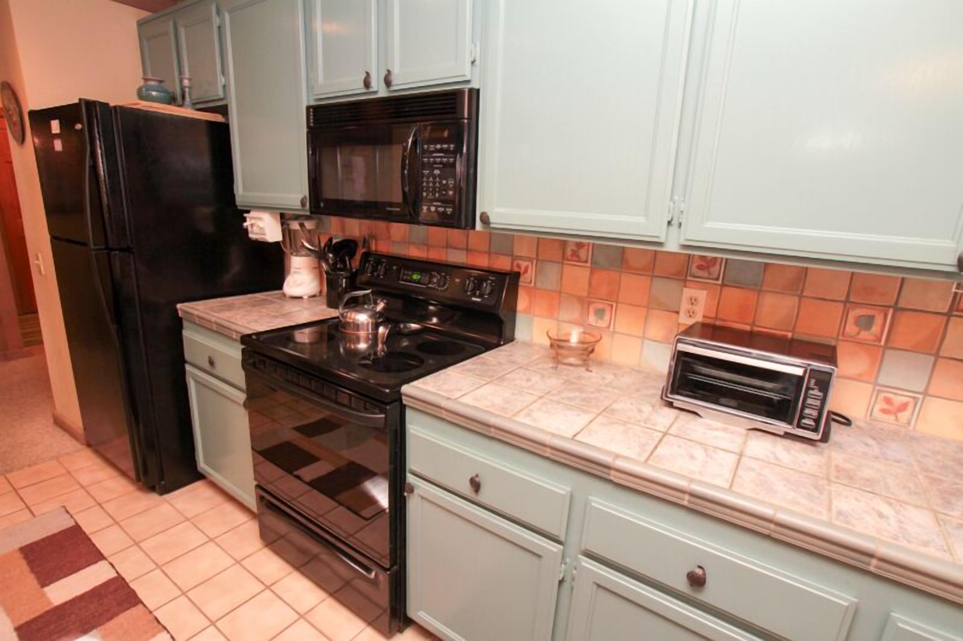 A kitchen with light blue cabinets, a black refrigerator, a stove, a microwave, and a toaster.