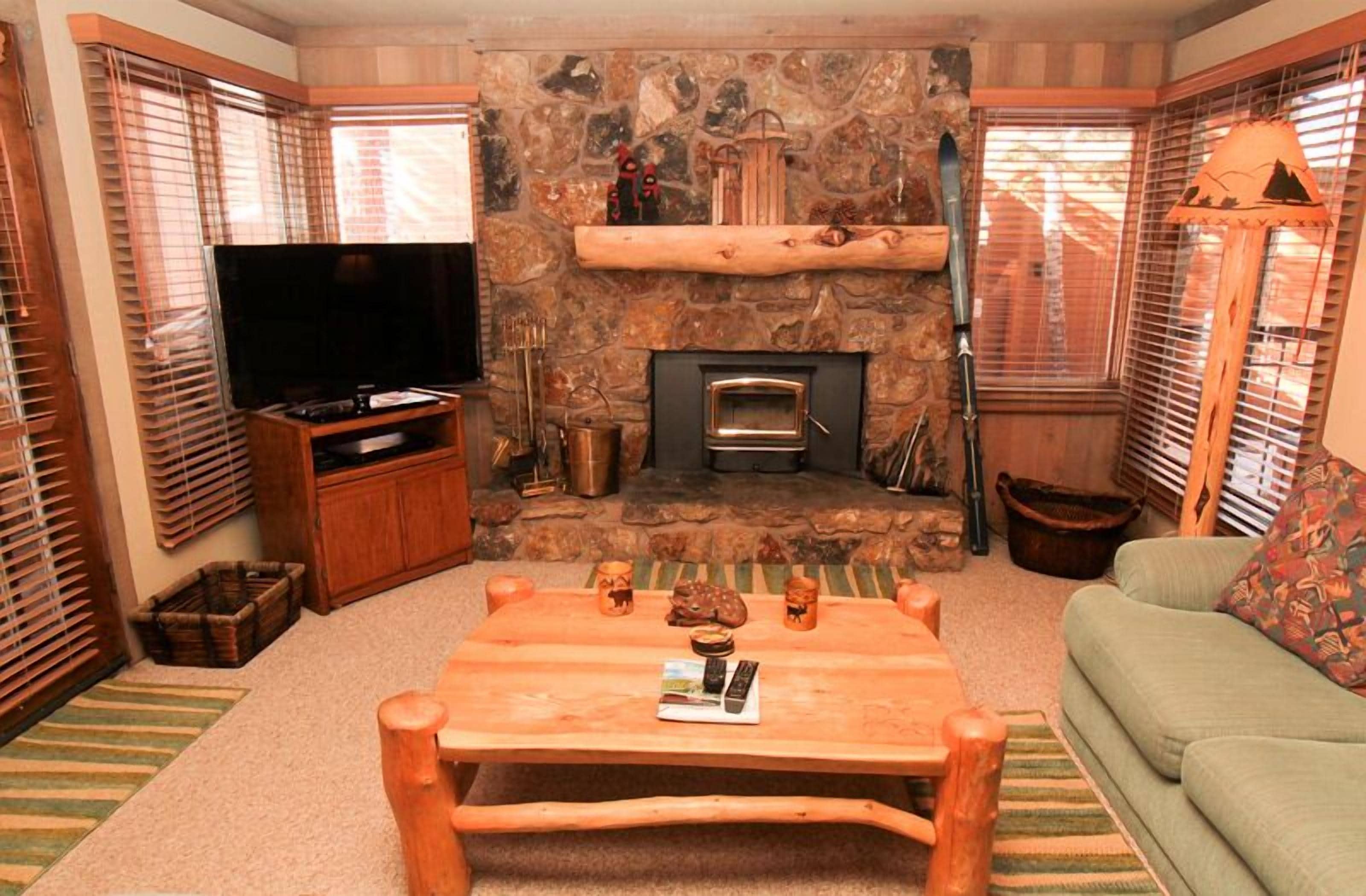 A cozy living room with a stone fireplace, a flat-screen TV, and a green sofa.