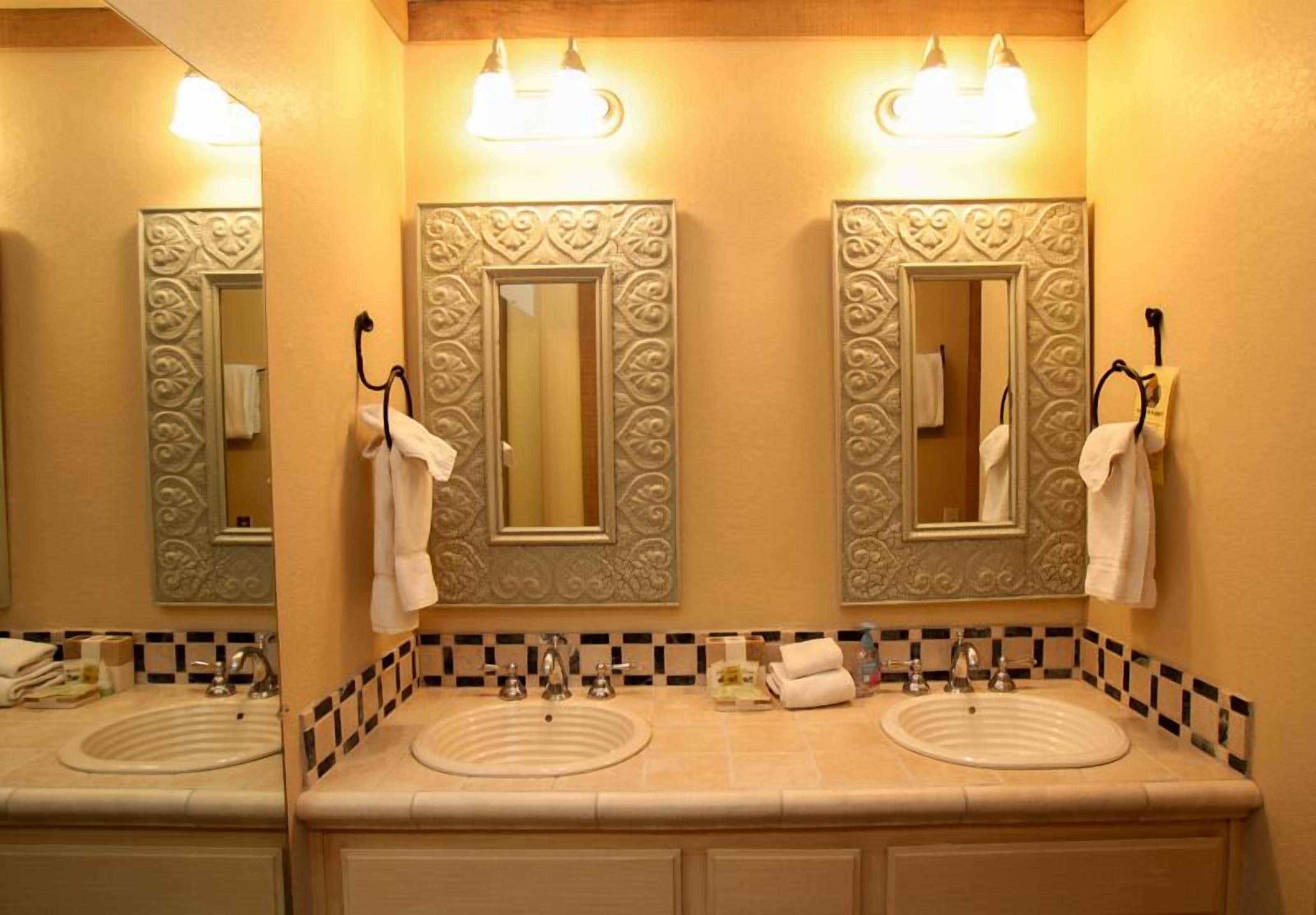 A bathroom with two sinks, each with a mirror above. There are towels hanging on hooks and a soap dispenser on the counter.