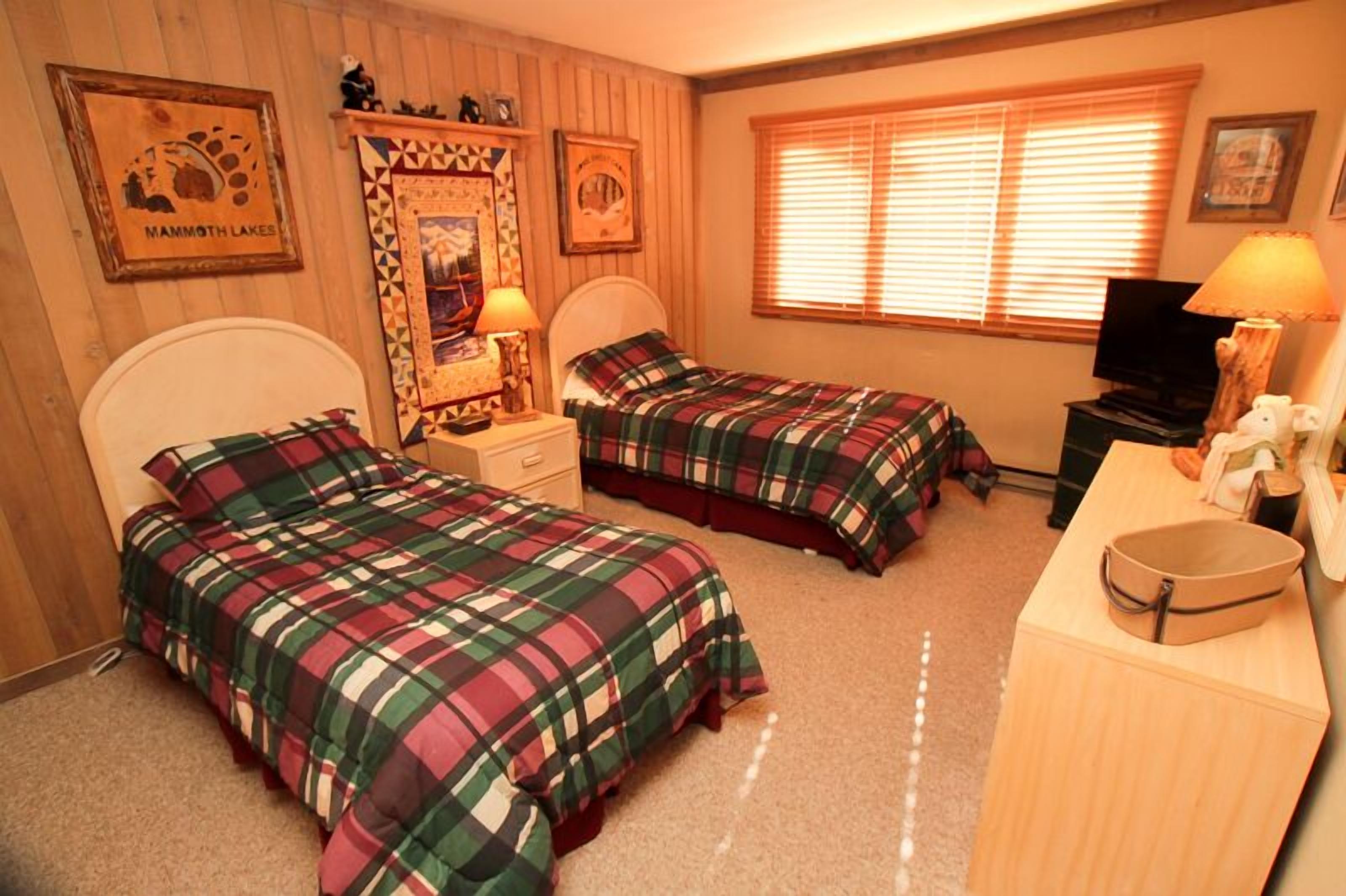 Een kamer met twee bedden, een bureau, een televisie en een raam met jaloezieën.
