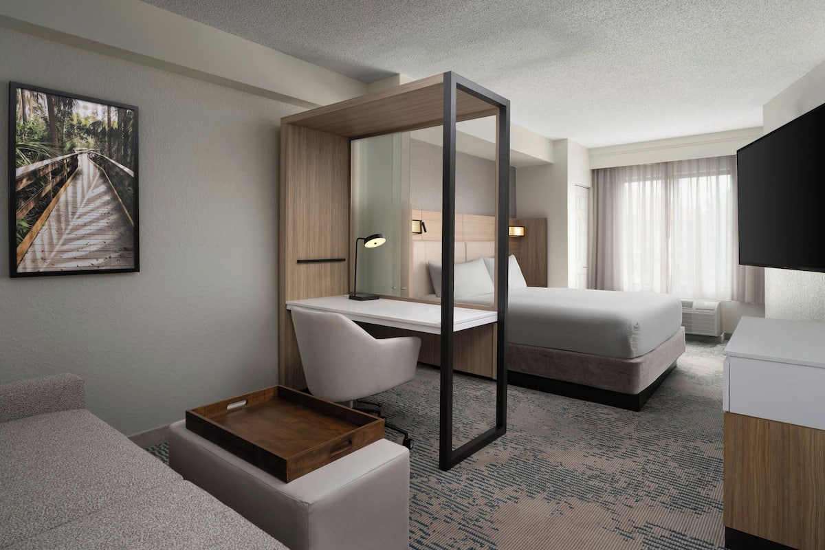 Une chambre d’hôtel moderne équipée d’un lit, d’un bureau, d’une chaise et d’un grand miroir.