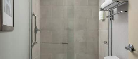 A shower with a glass door, a toilet, and a towel rack with folded towels.