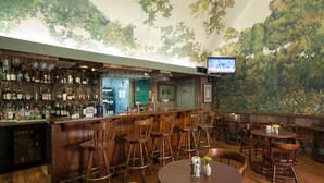 Un espace bar avec des meubles en bois, un téléviseur fixé au mur et une fresque représentant des arbres.