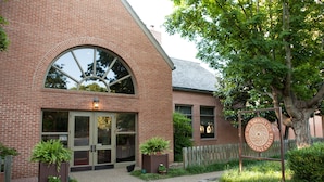 Un bâtiment en briques doté d’une grande fenêtre en arc de cercle, d’une enseigne indiquant le « New Harmony Inn Conference Center » et de plantes en pot devant l’entrée.