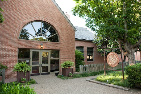 A brick building with a large arched window, a sign for the New Harmony Inn Conference Center, and potted plants in front.