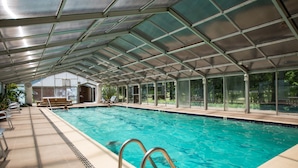 Une piscine intérieure avec des parois en verre transparent, une terrasse carrelée et un toit abrité.