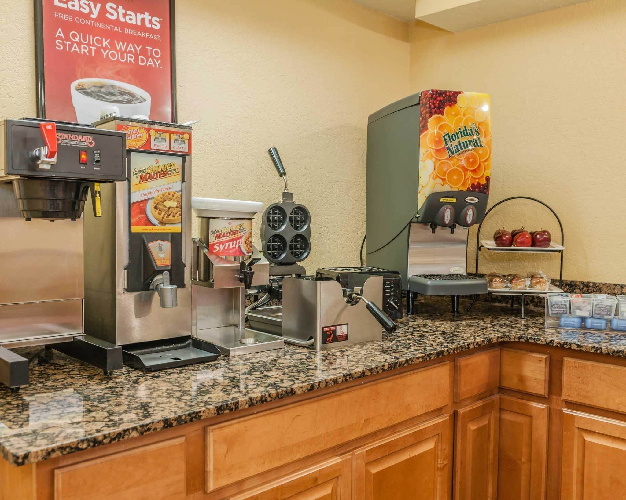 A breakfast bar with a coffee machine, waffle maker, and juice dispenser.