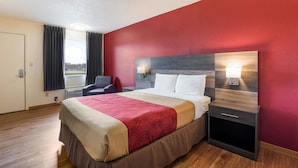 Habitación de hotel con una cama grande, una mesita de noche, una silla, una ventana con cortinas y vistas a la ciudad.