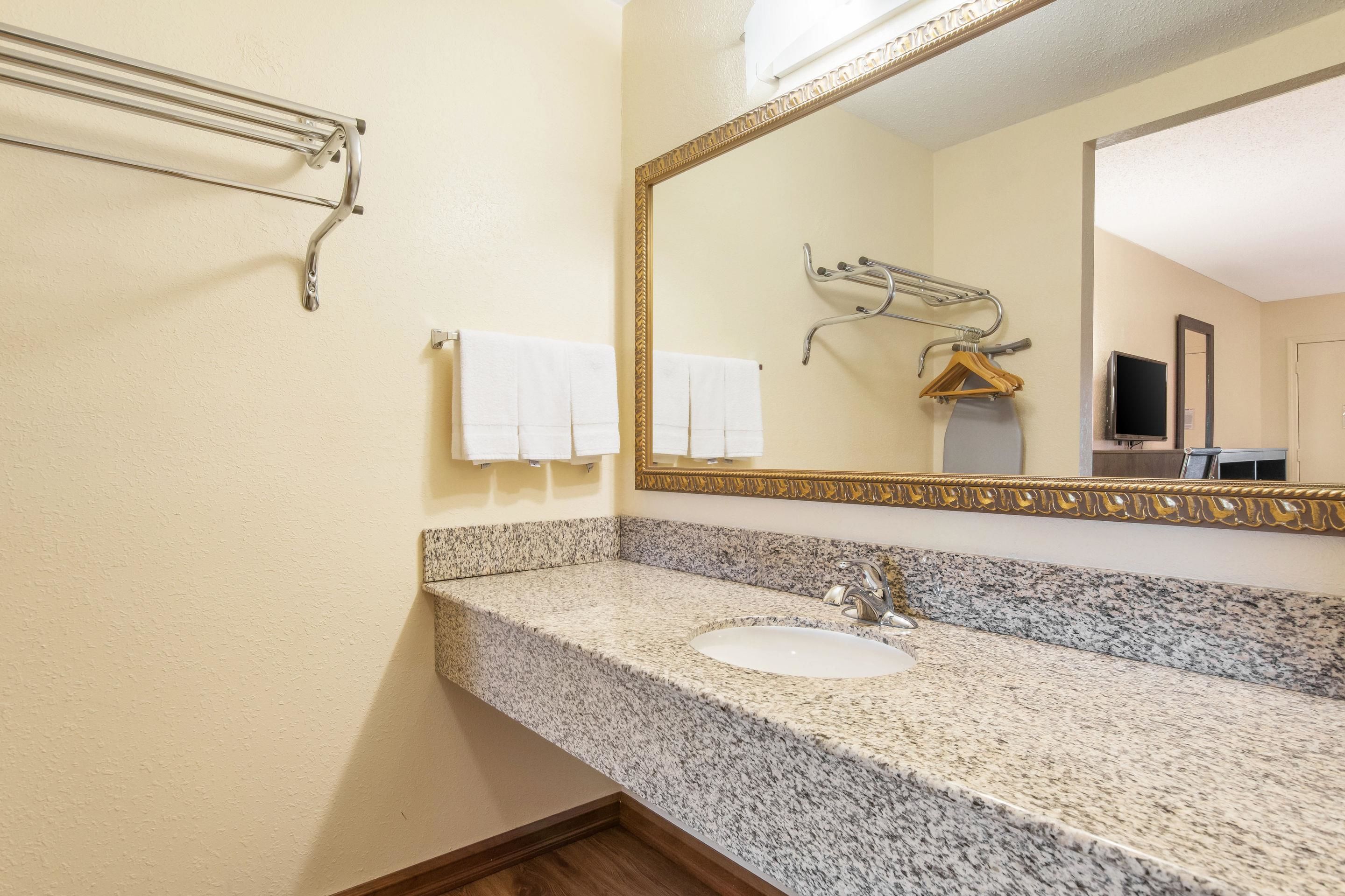 A bathroom with a granite countertop sink, a gold-framed mirror, and a towel rack with white towels.
