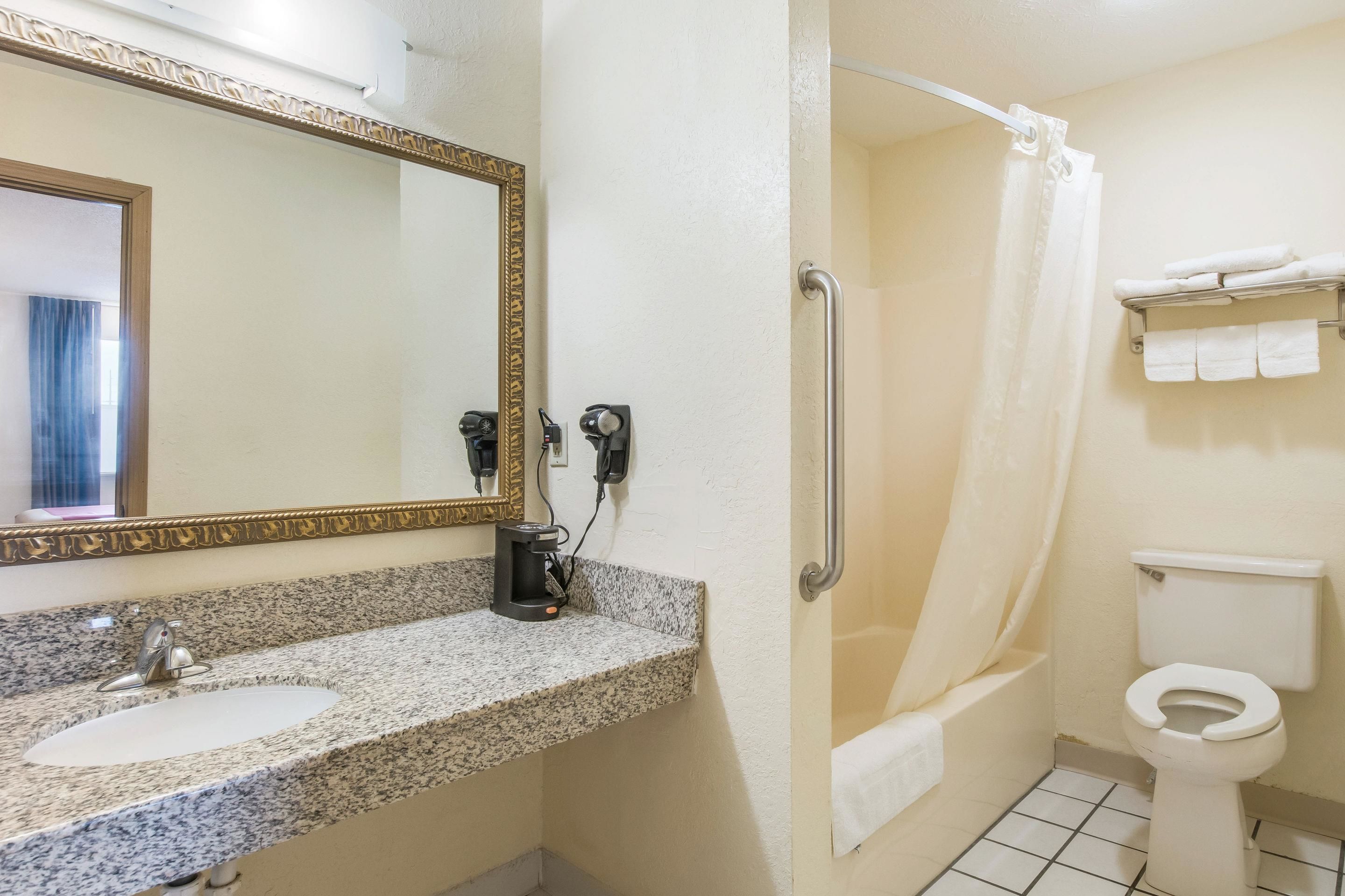 A bathroom with a granite countertop sink, a mirror with a gold frame, a shower with a white curtain, and a toilet with a towel rack.