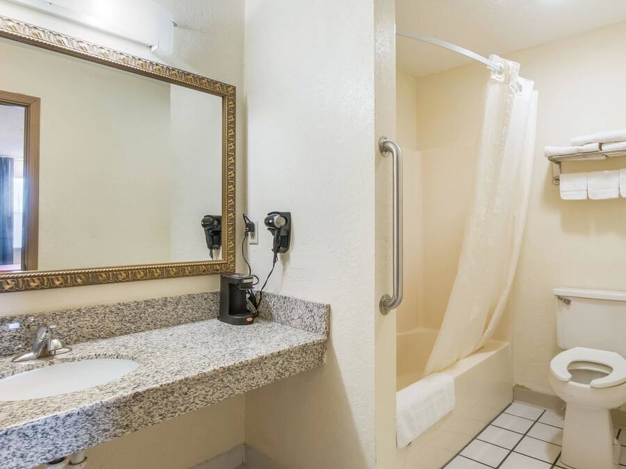 A bathroom with a granite countertop sink, a mirror with a gold frame, a shower with a white curtain, and a toilet with a towel rack.