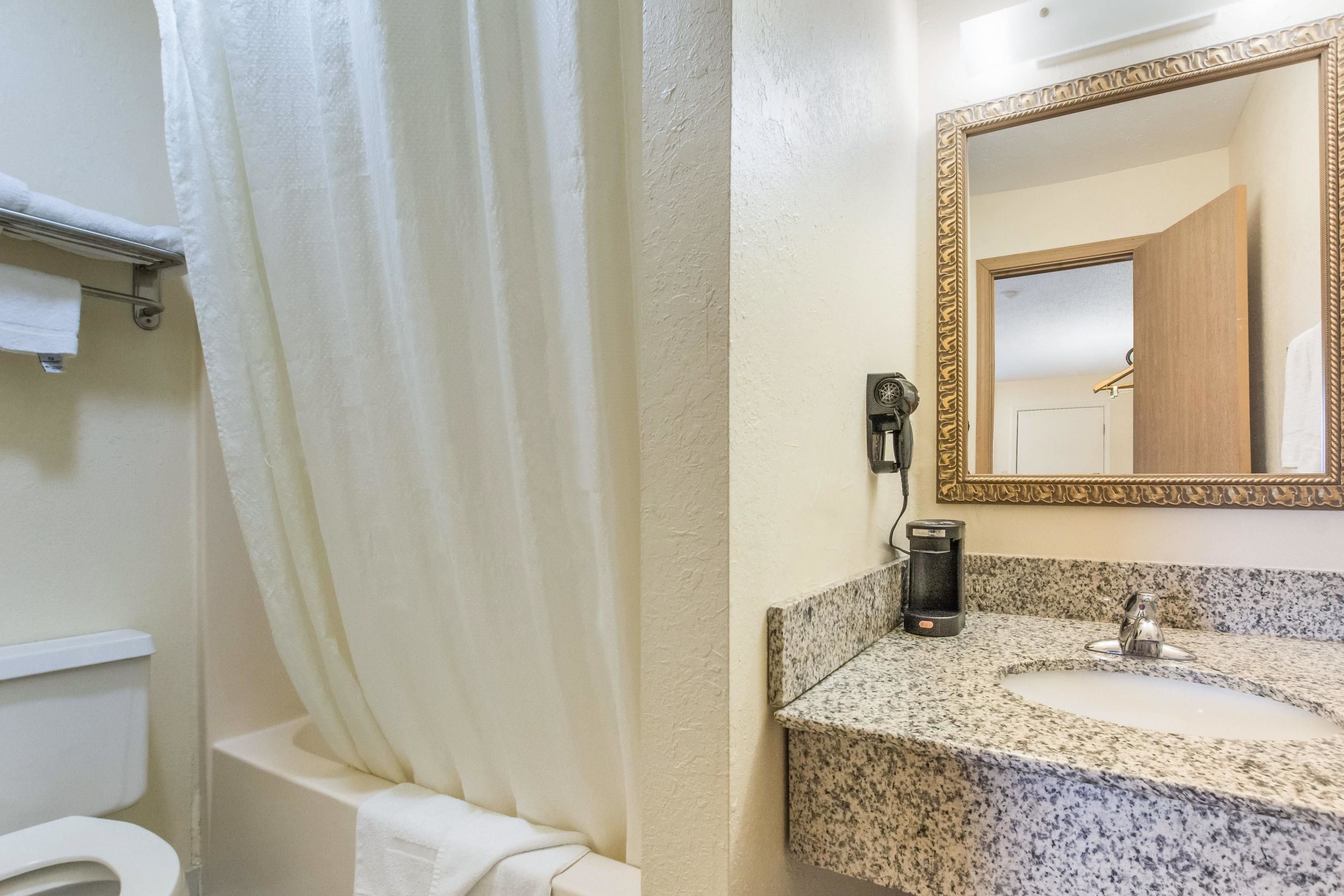 Un baño con cortina de ducha, inodoro, lavabo con encimera de granito y espejo con marco decorativo.