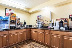 A commercial kitchen with various coffee machines, a refrigerator, and a display of breakfast items. - Econo Lodge Cloverdale (Cloverdale)