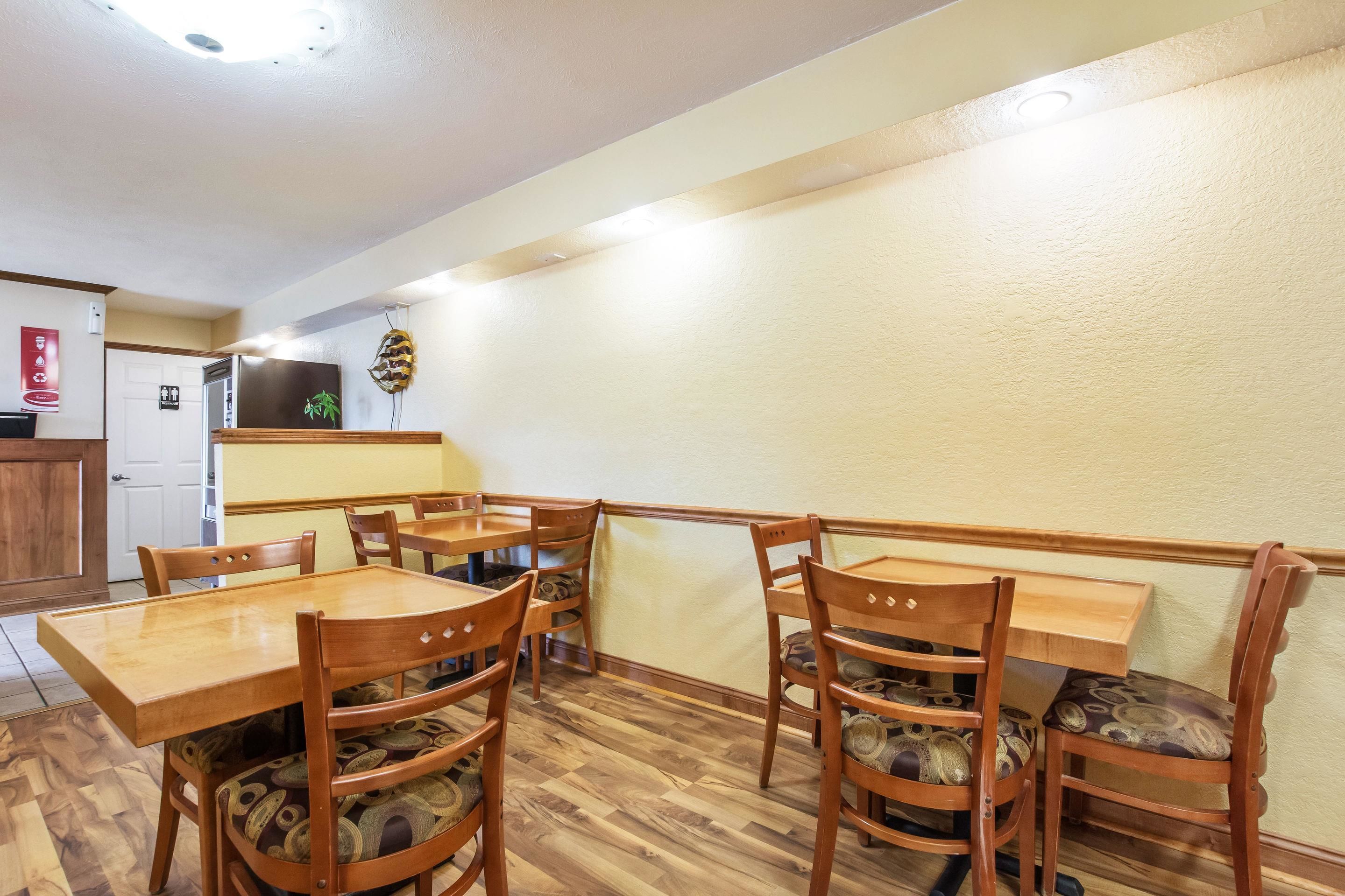 Un comedor con mesas y sillas de madera, una cocina al fondo y un techo con iluminación empotrada.