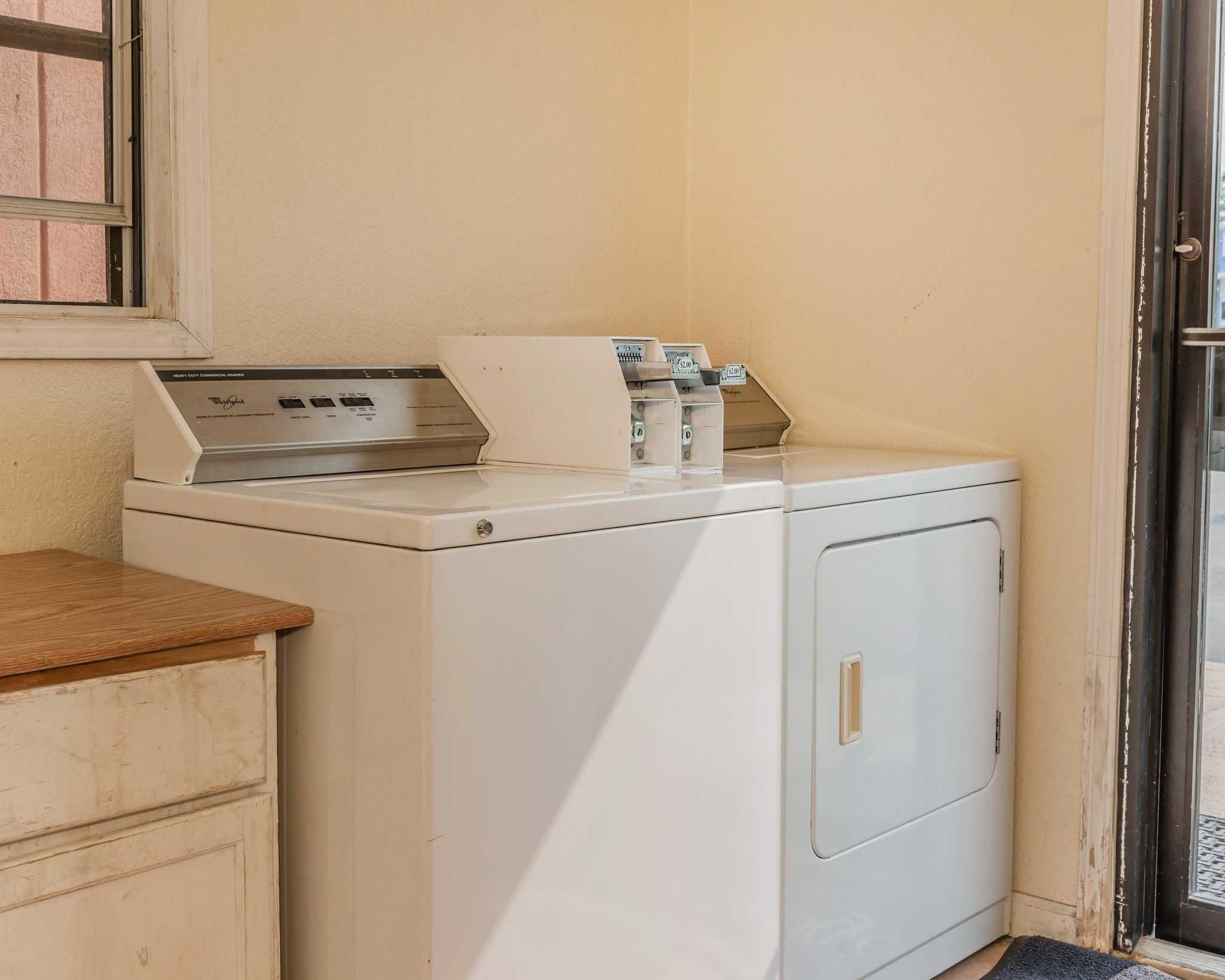 A laundry area with a front-loading washer and dryer, a wooden counter, and a window above the washer.