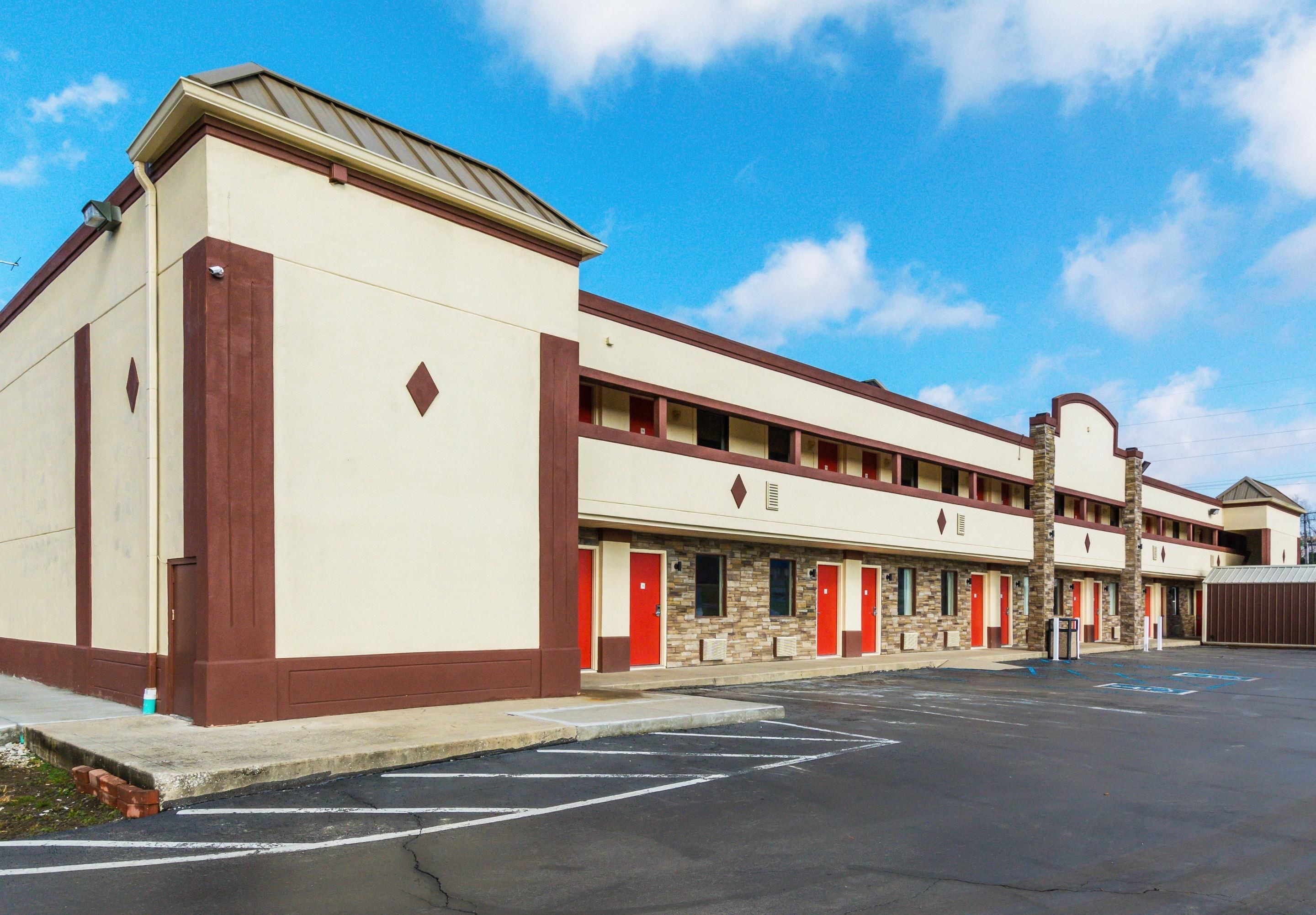 A motel with a row of rooms, each with a red door and a small window above the door. The building has a beige exterior with brown trim.
