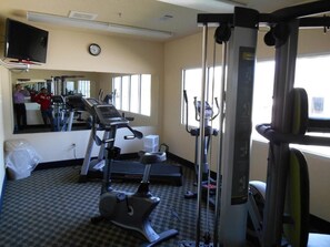 A gym with exercise equipment, a mirror, and a clock on the wall.