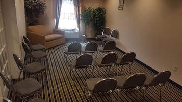 A hotel room with a striped carpet, a sofa, and several chairs arranged for a meeting or conference.