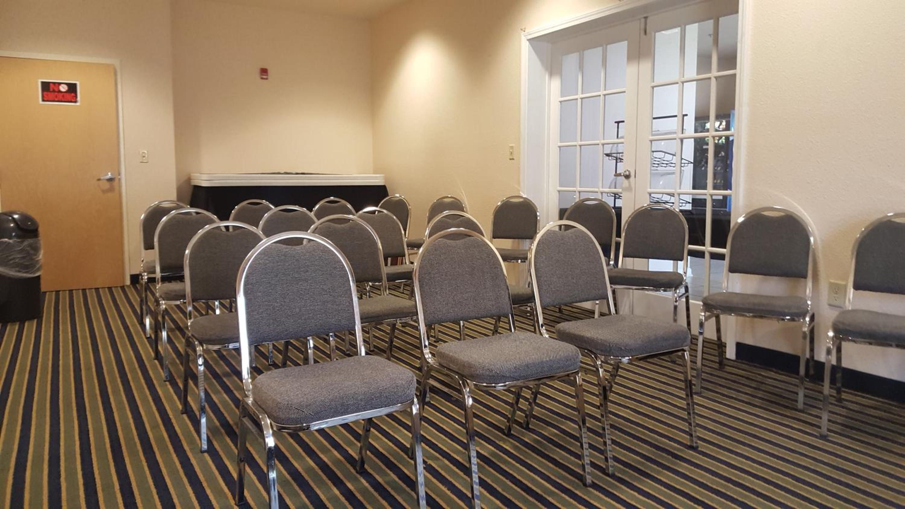A conference room with rows of chairs, a door with a 'No Smoking' sign, and a window with blinds.