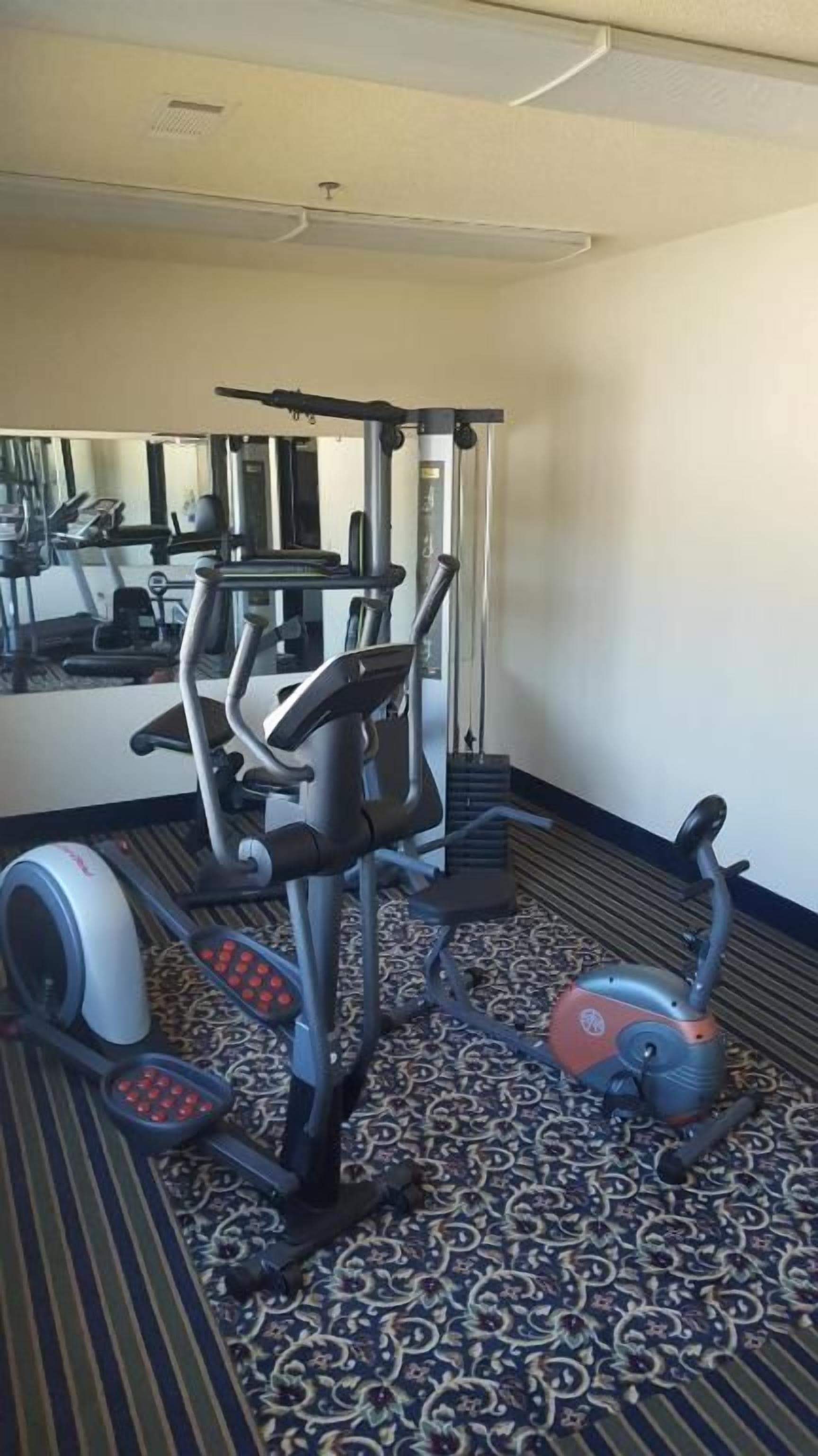 A hotel gym with exercise equipment, including a treadmill, elliptical, and weight machine.