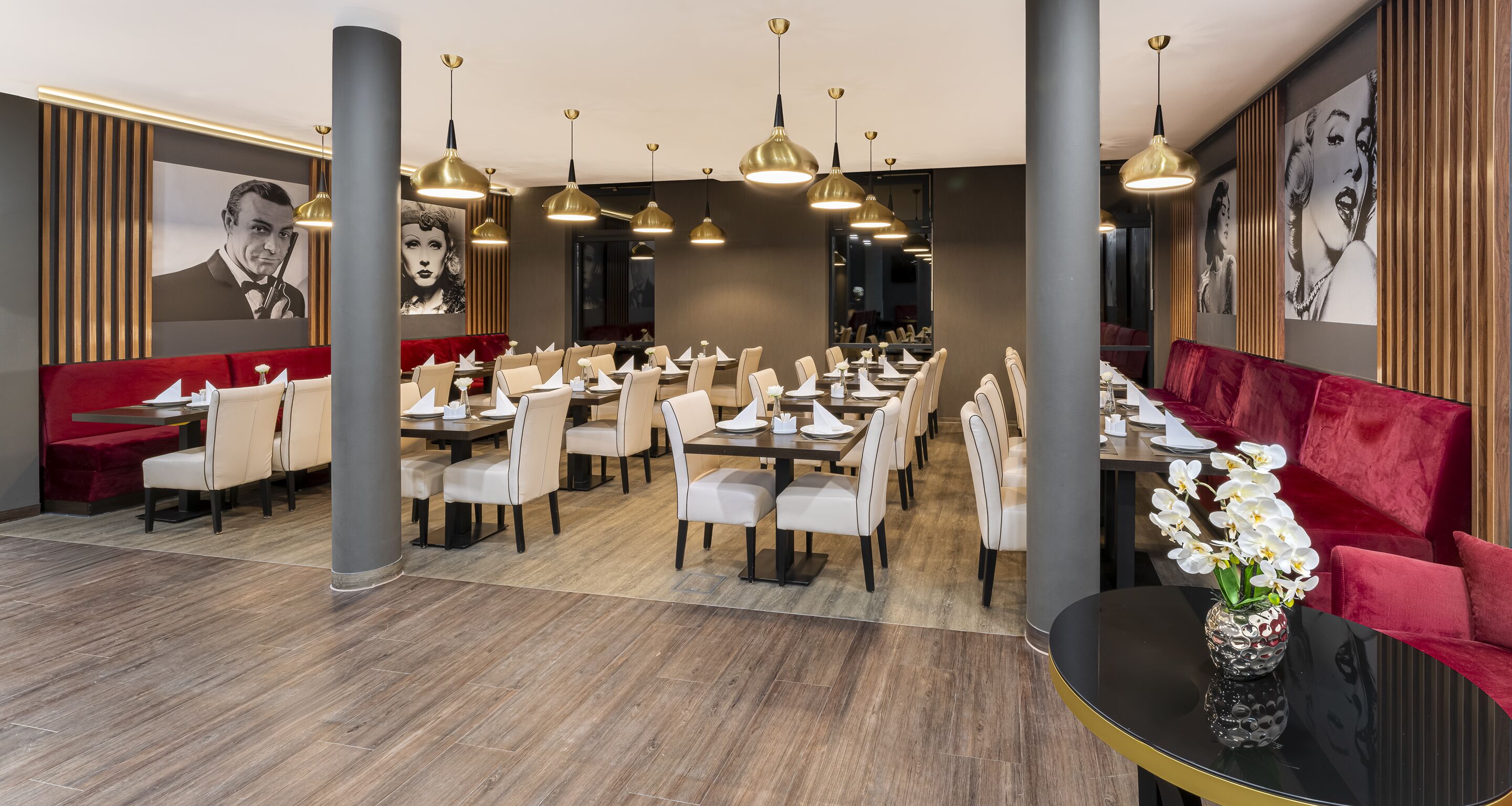 A restaurant with multiple dining tables and chairs, red upholstered booths, and hanging pendant lights.