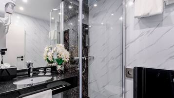 A modern bathroom with a black marble sink, a glass shower enclosure, and white marble walls.